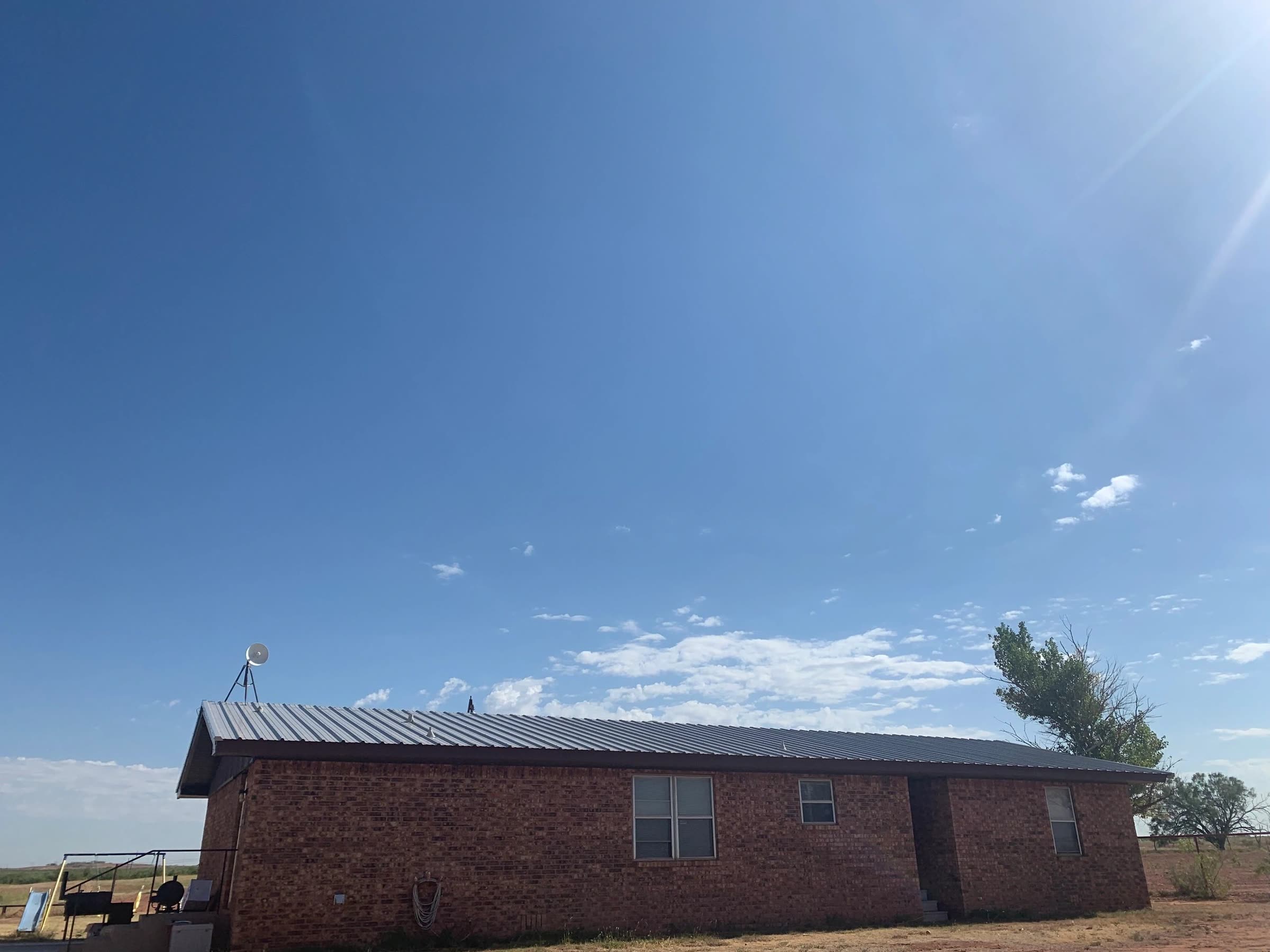 Brick ranch house with a new metal roof under a wide West Texas sky