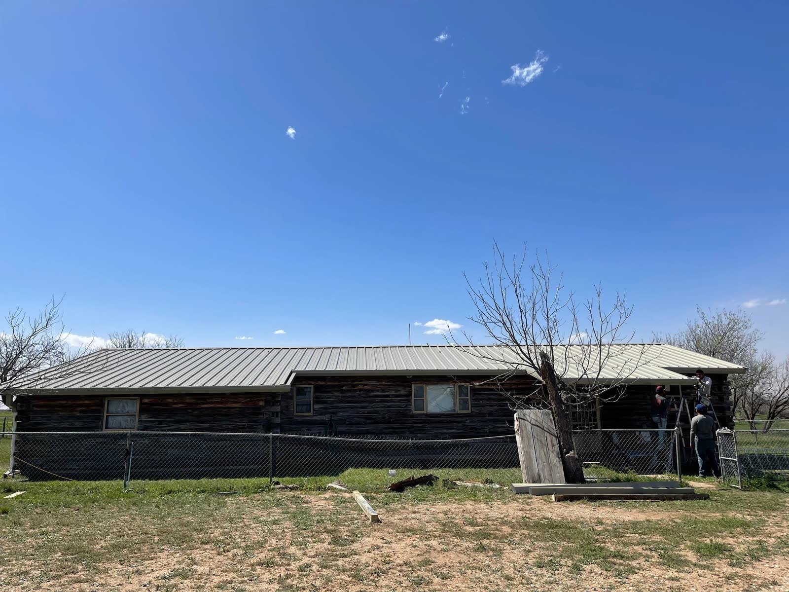 Long ranch house with dark siding and a new metal roof, crew at the far end