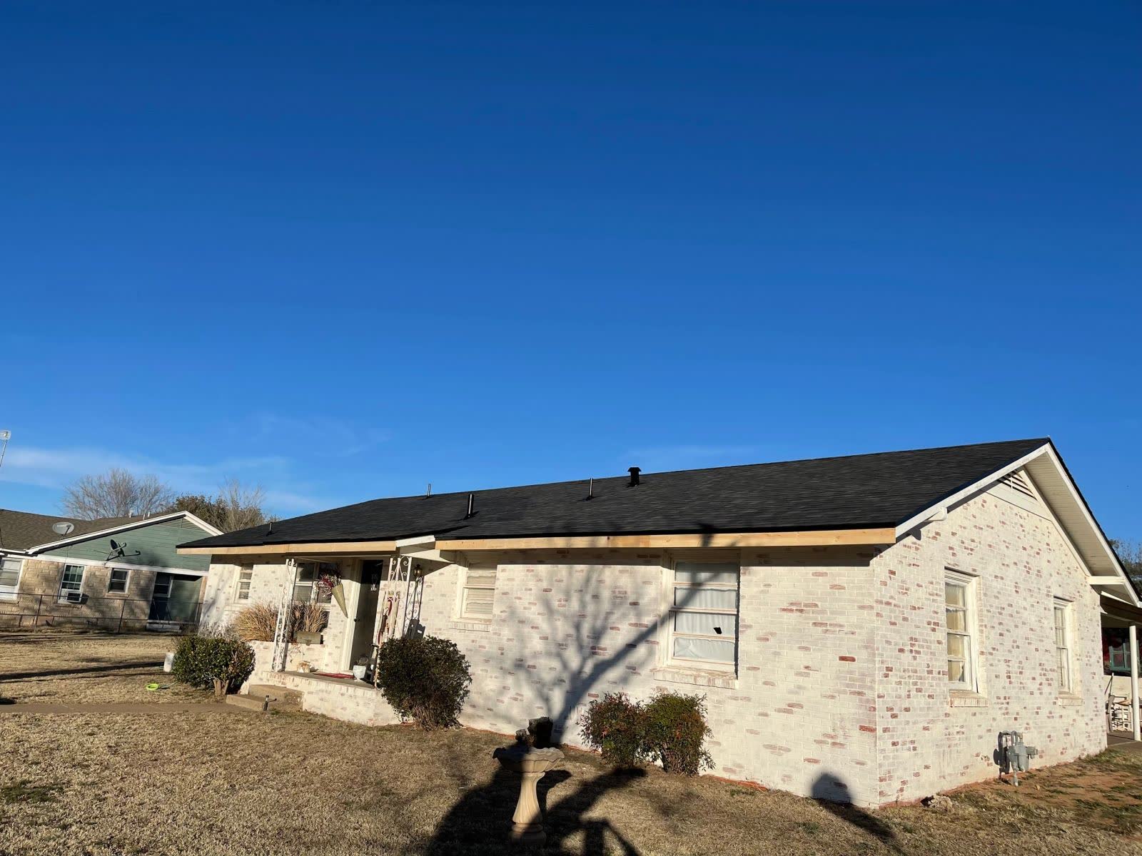 White stone ranch house with a new dark shingle roof